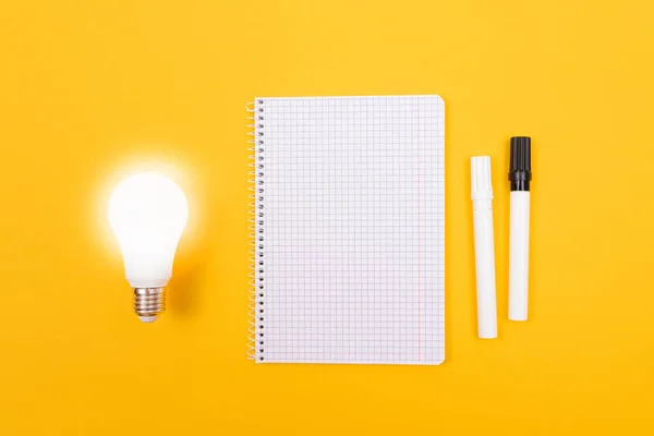 Glowing Power Saving Lamp with Notepad Lying on Yellow Table