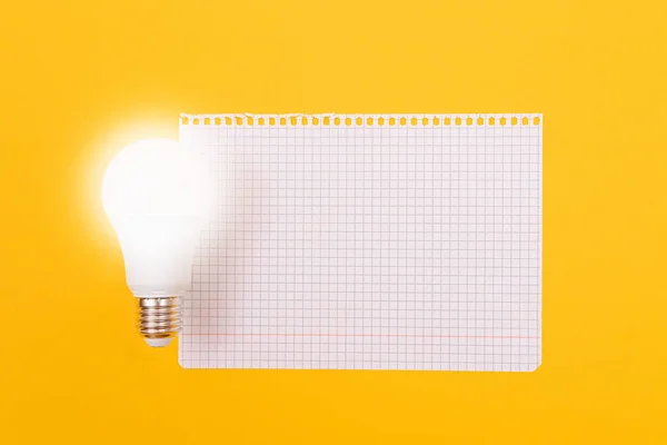 En energisparlampa med anteckningsblock liggande på gult bord — Stockfoto