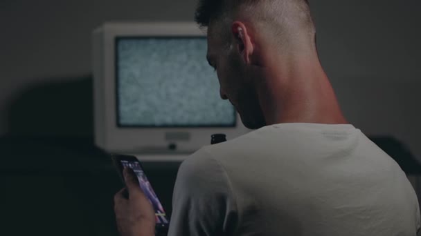 Muž v bílém tričku sedí proti staré stříbrné TV — Stock video