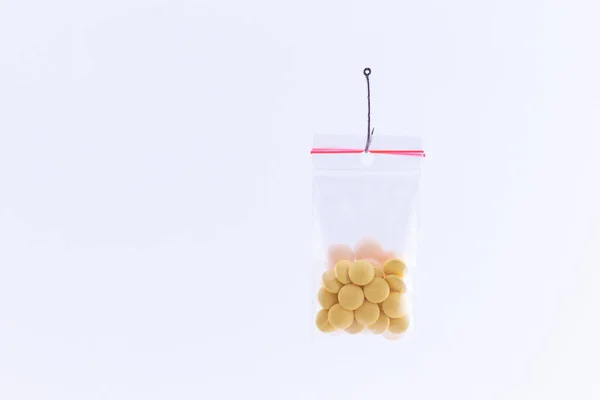 Farbige Pillen oder Tabletten hängen in einer kleinen Reißverschlusstasche am Angelhaken — Stockfoto