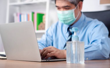 Maske takan bir işadamı masasında el dezenfektanı ya da antibakteriyel hijyen ve Coronavirüs hastalığı için maskesiyle duruyor..