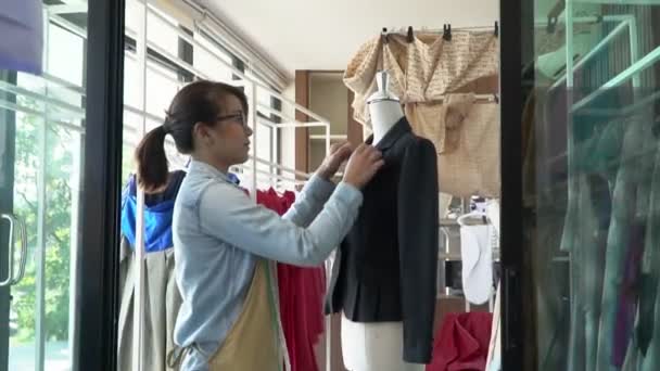 Ευτυχισμένη νεαρή ασιατική γυναίκα μοδίστρα σχεδιαστής μόδας ελέγχει για την ολοκλήρωση για ένα κοστούμι και φόρεμα σε ένα εκθεσιακό χώρο. Έννοια της επιτυχίας νεαρός επιχειρηματίας στην επιχείρηση μόδας. — Αρχείο Βίντεο