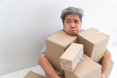 Kurye eve teslim edildikten sonra Asyalı Alışverişkolik adam şok oldu ve oturma odasında yerde ve üzerinde karton kutu oturdu. İnternetten alışveriş ve alışveriş kavramı.