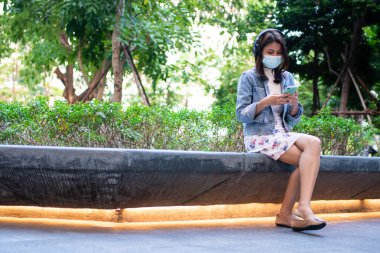 Anti-koronavirüs COVID-19 salgın hastalıkları için maske takmış genç bir kadının portresi ve halka açık alanda akıllı telefon kullanımı. Virüs salgını ve kirliliği kavramı
