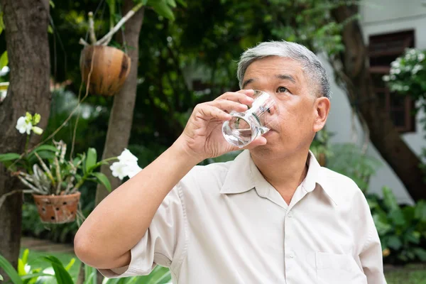 senior old man reading a book in the park and drinking water. Concept of retirement lifestyle and hobby.