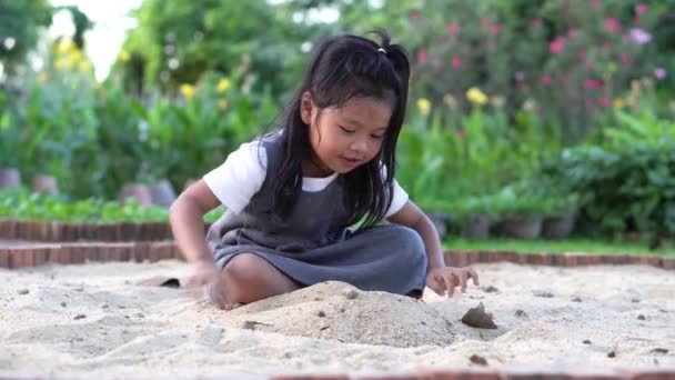 Liten asiatisk flicka sitter i sandlådan och spelar whit leksak spade hink och hon skopade i leksak spade hink. Leka är en lärande utveckling och bygger muskler för barn. — Stockvideo