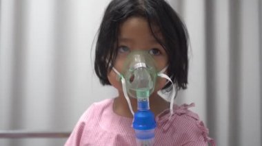 Küçük Asyalı kız oksijen maskesi takıyor ve hastanede nebulizatörle nefes alıyor. Bronşit, solunum ve tıbbi tedavi kavramı.