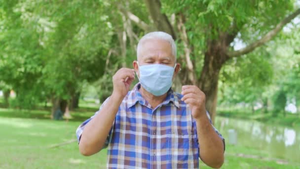 Az idős ázsiai férfi arcképe, amint maszkot vesz le a parkban, miután a járvány megoldódott, miután rendelkezésre állnak oltóanyagok és gyógyszerek.. — Stock videók