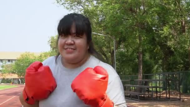 Mujer asiática con sobrepeso feliz usa guantes de boxeo rojos Trata de perder peso haciendo ejercicio en el jardín golpeando. Concepto de salud y pérdida de peso a través del ejercicio. — Vídeos de Stock