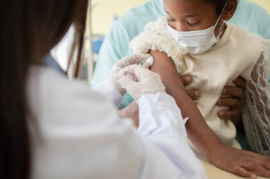 Enjeksiyon için Asyalı doktor şırınga iğnesi, Afrika kökenli Amerikalı çocuklar koronavirüsü ve gribi önlemek için aşılanıyorlar. Aşıdan gelen bağışıklık kavramı