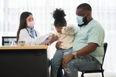 Enjeksiyon için Asyalı doktor şırınga iğnesi, Afrika kökenli Amerikalı çocuklar koronavirüsü ve gribi önlemek için aşılanıyorlar. Aşıdan gelen bağışıklık kavramı