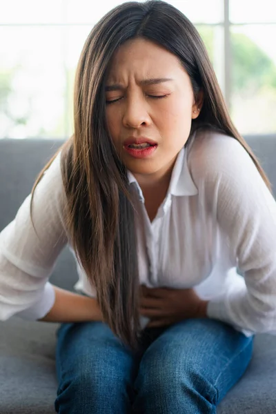 不幸なアジアの女性は ソファの上に座って 胃の苦しみを保持します または消化不良による腹痛 病気と医療の概念 — ストック写真