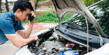Kızgın Asyalı bir adam ve caddedeki bir araba arızasından sonra yardım için cep telefonu kullanıyor. Araç motoru sorunu veya kaza kavramı ve profesyonel tamirciden acil yardım