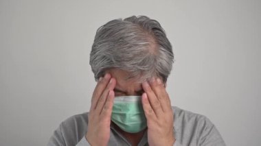 Tıbbi maske takan hasta Asyalı bir adam ve baş ağrısını tutmak için elini uzat. Korunma pandemik koronavirüs ve solunum hastalığı kavramı