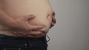Aşırı kilolu adama yaklaşmak, şişmanlığın büyük bir göbek olduğunu gösteriyor. Şişman karnına dokunan obez bir adamın elleri. Göbek yağlarının yavaşça sallanması