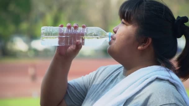 Mujer asiática con sobrepeso bebiendo agua para una botella en el estadio después de correr por la mañana. Concepto de cuidado de la salud mediante el ejercicio y beber agua limpia — Vídeos de Stock