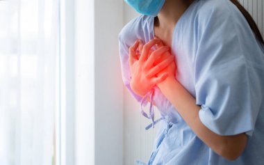 Kalp krizi belirtilerinden dolayı maske takan ve göğsünü tutan bir kadın hasta.