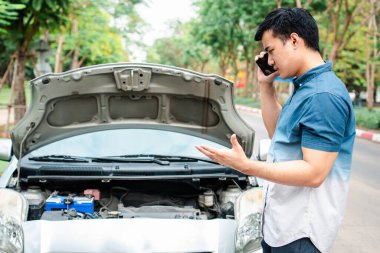 Kızgın Asyalı bir adam ve caddedeki bir araba arızasından sonra yardım için cep telefonu kullanıyor. Araç motoru sorunu veya kaza kavramı ve profesyonel tamirciden acil yardım
