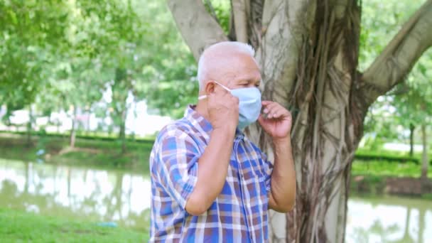 Porträt eines älteren asiatischen Mannes, der im Park die Gesichtsmaske abnimmt, nachdem sich die Epidemie nach der Verfügbarkeit von Impfstoffen und Medikamenten gelöst hat. — Stockvideo