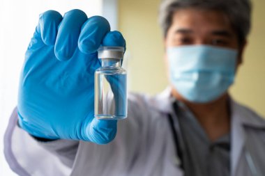 Asyalı bir erkek doktor, hasta için antikor örneklerini incelemek ve analiz etmek için kovid 19 koronavirüs aşısı alan tıbbi eldiven ve yüz maskesi takıyor. Hastalık kavramı, tıbbi bakım