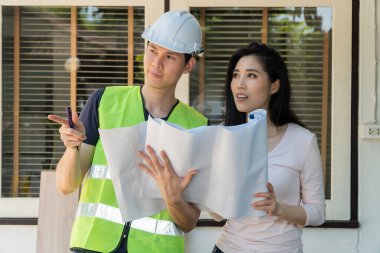 Asyalı profesyonel mimar elinde proje tutuyor ve ev dekorasyonu ve konut inşaatı, mimari ve iç mimari konsepti tasarımı için ev sahibiyle ilgili planı anlatıyor.