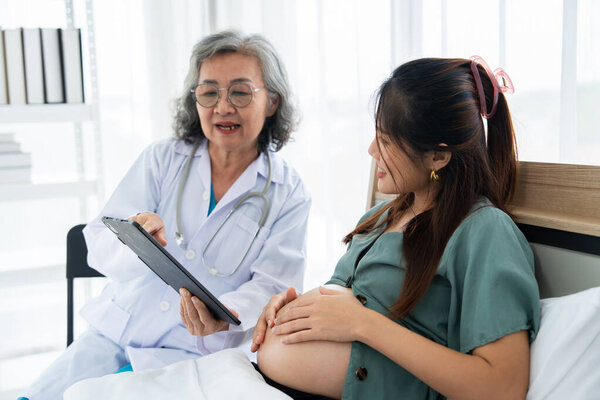 Беременная женщина сидит на больничной койке во время пренатальной консультации с улыбающимся врачом. Сцена подчеркивает материнское здоровье, профессиональный уход и поддерживающее общение в клинике.