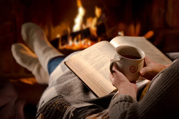 Vrouw leest boek in de buurt van open haard — Stockfoto