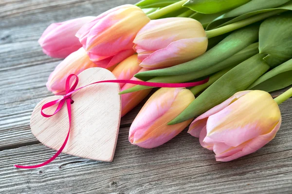 Tulipanes coloridos y corazón sobre fondo de madera —  Fotos de Stock