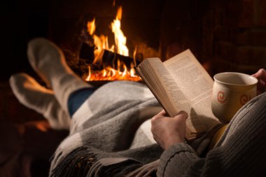 Woman reads book near fireplace clipart