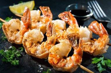 Soya soslu ızgara karides şişleri, sarımsak, taze maydanoz ve limonlu siyah tabak.