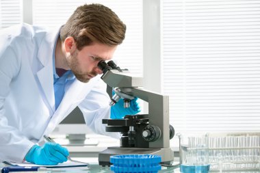 Bilim adamı mikroskopla bakıyor.