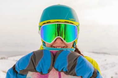 Bir snowboardcu dağların panoramasında bir yamaçta poz veriyor. Dağdan inmeye hazırlanıyor..