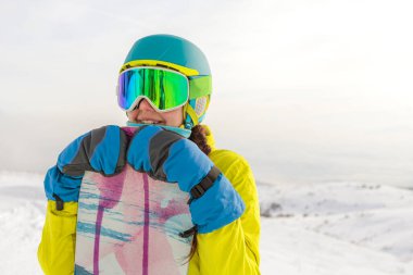 Bir snowboardcu dağların panoramasında bir yamaçta poz veriyor. Dağdan inmeye hazırlanıyor..