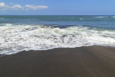 Endonezya 'nın Bali kentindeki siyah bir kumsal sahili üzerinde bir dalga dolaşır. Bali, Endonezya' daki siyah kum volkanik plajı.