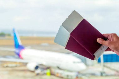 Havaalanından kalkış ve varış için bilgi panosunun karşısındaki bir kadının elinde kırmızı renkli iki pasaport ve biniş kartı..