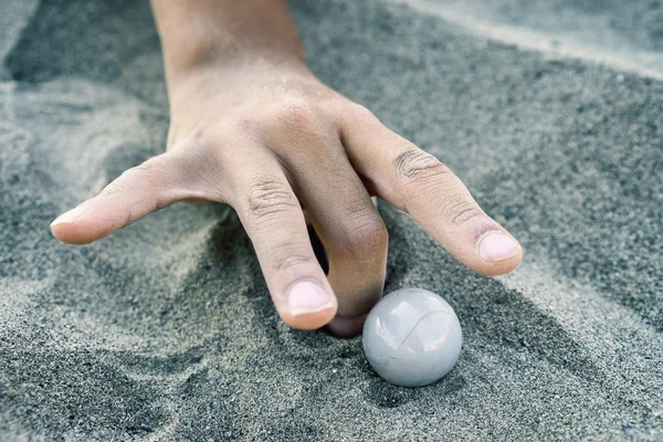 hand of a child playing with marbles in the sand