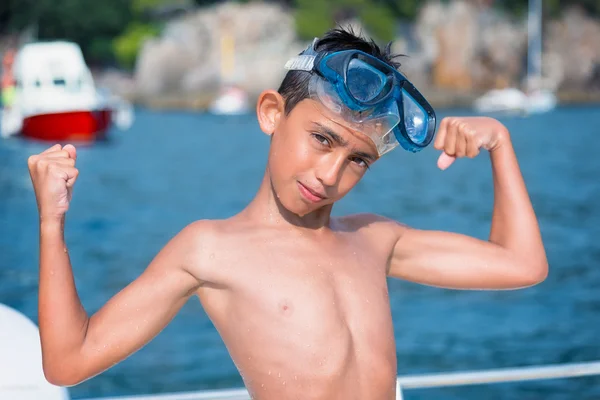 Liten pojke med scuba mask visar musklerna på havet — Stockfoto