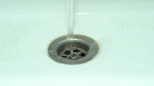 Agua clara fluye por el orificio de drenaje en el fregadero blanco en el drenaje — Vídeos de Stock