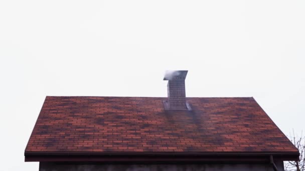 Rook komt uit een bakstenen schoorsteen van een klein prive-huis met een mooie bruine bitumen dakpan — Stockvideo