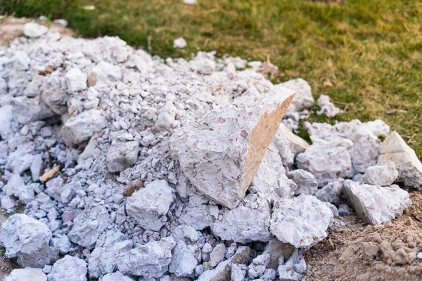 A mountain of construction waste made of concrete stones of different sizes against the background of a green lawn. Removal of construction waste to the landfill