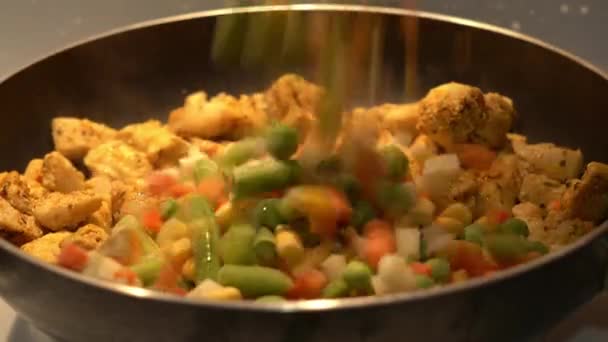Frysta grönsaker hälls i en kastrull med stekt kyckling — Stockvideo