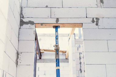 Bir inşaat krikosu tamamlanmamış bir evde beyaz bir beton bloğu destekliyor.