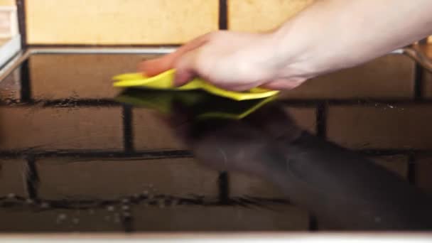 Afvegen van de zwarte glanzende elektrische kachel met een gele doek — Stockvideo