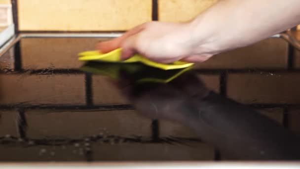 Wiping the black glossy electric stove with a yellow rag — Vídeos de Stock