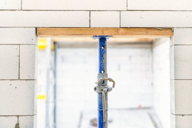 Bir inşaat krikosu tamamlanmamış bir evde beyaz bir beton bloğu destekliyor.