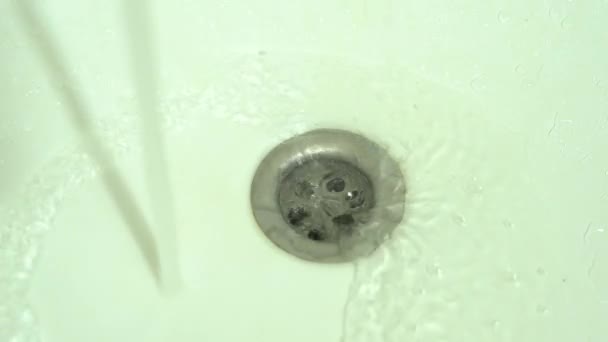 Wasser fließt in ein Abflussloch in einer weißen Keramikspüle, Nahaufnahme — Stockvideo