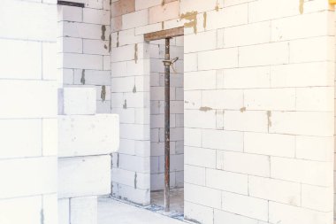 Bir inşaat krikosu tamamlanmamış bir evde beyaz bir beton bloğu destekliyor.