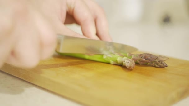 Ręce wyciąć zielone szparagi z nożem na drewnianej tablicy zbliżenie — Wideo stockowe