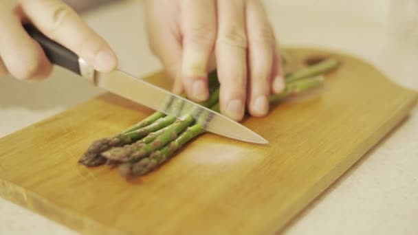 Tagliare gli asparagi verdi crudi prima di cuocerli su una tavola di legno — Video Stock