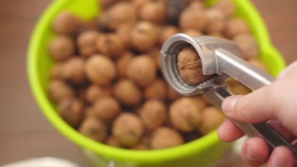 Nutcracker in hand and walnut close-up against the background of a bucket with nuts — Stock Video